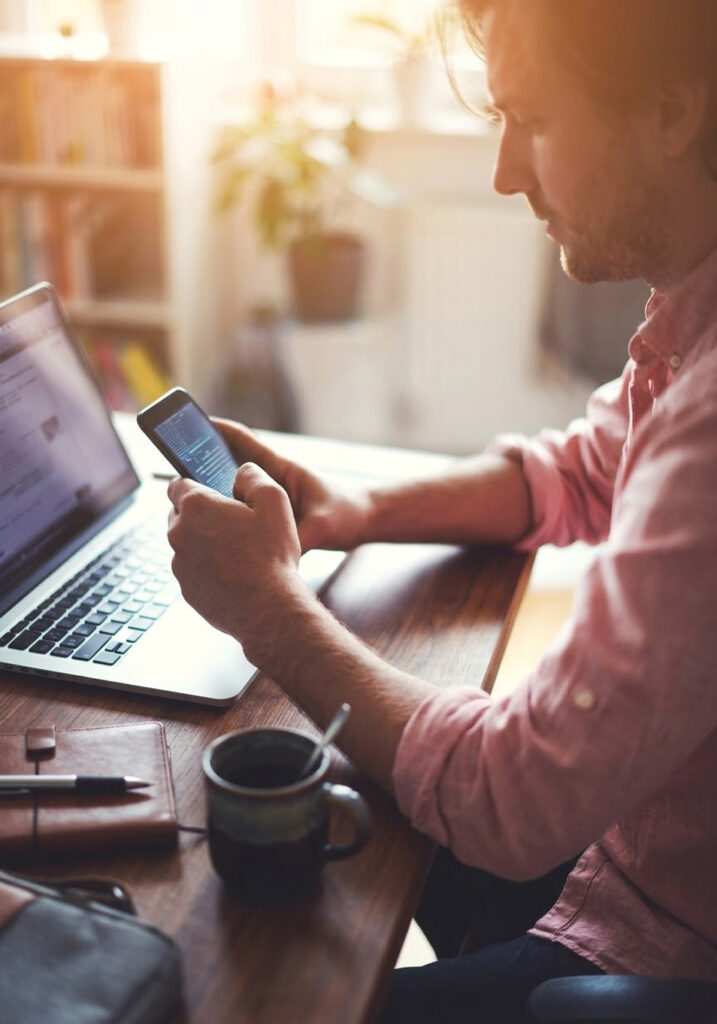 An image of a person holding his phone while he is on his laptop